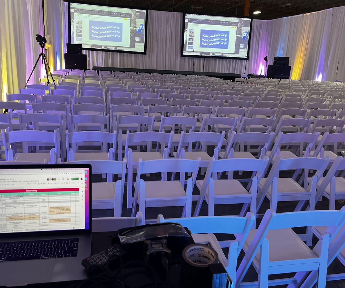 White chairs set up nicely facing 2 large projector screens for Business event. 